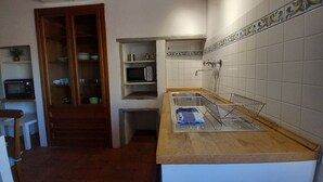 A compact kitchen with a wooden countertop, a built-in microwave, a sink with a drying rack, and a cabinet with glass doors.