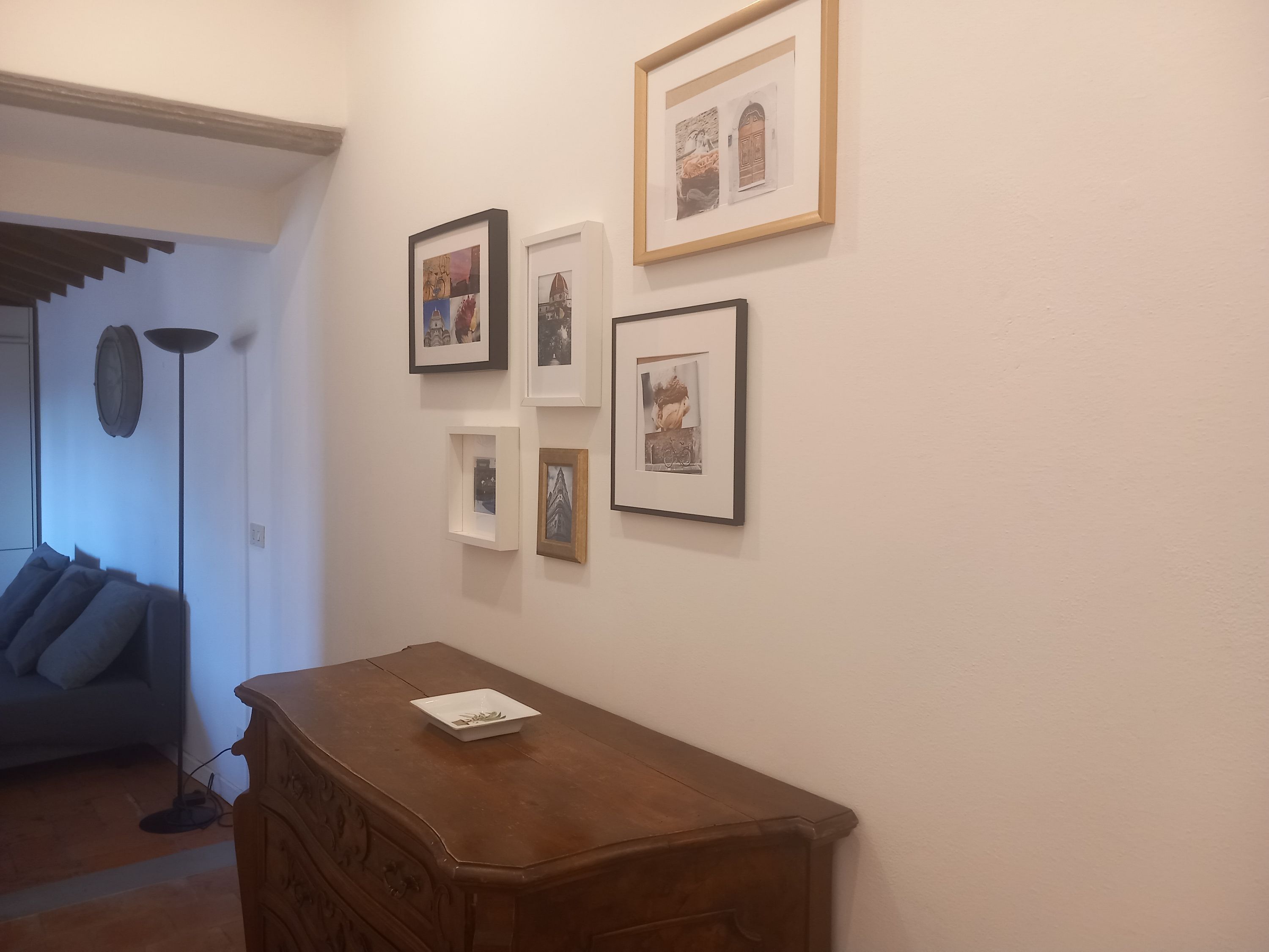 Een kamer met een houten dressoir, een lamp en diverse ingelijste foto’s aan de muur.