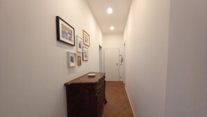 A narrow hallway with a wooden dresser against the wall, a door at the end, and several framed pictures on the wall.
