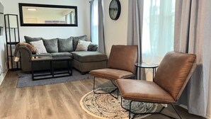 En moderne stue med en hjørnesofa, en læderarmstol i brunt, et lille rundt bord og en tæppe med et mønster.