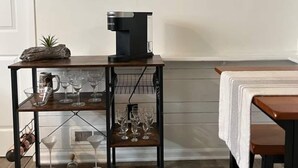 Spiseområde med et træbord, en kaffemaskine og en hylde med køkkenudstyr.