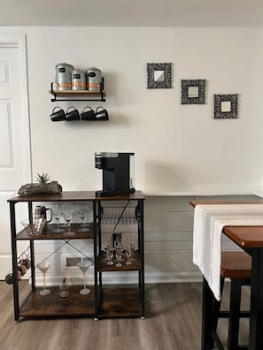 Zona pranzo con tavolo in legno, macchina da caffè e ripiano con stoviglie.