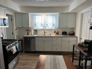Una cucina compatta con lavastoviglie, piano cottura e finestra ornata da un pannello decorativo.