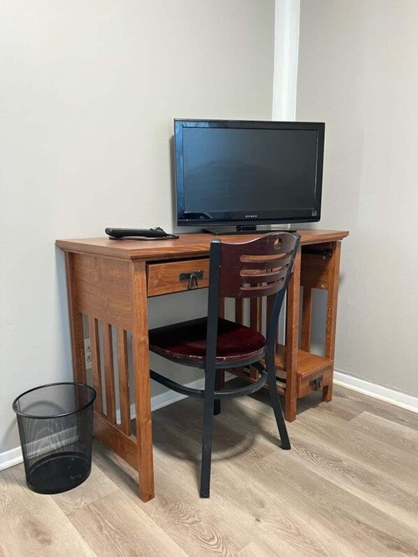 A wooden desk with a computer monitor, a chair, and a trash can.
