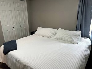 A bed with white bedding, a dark throw blanket, and a white door in the background.