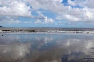 Una playa con arena mojada y mar tranquilo.