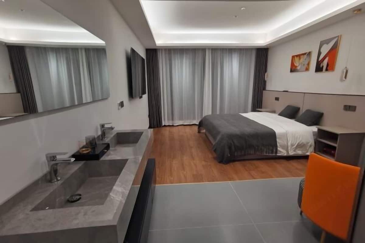 A modern hotel room with a large bed, a built-in desk, a large mirror, a vanity with a sink, and a shower.