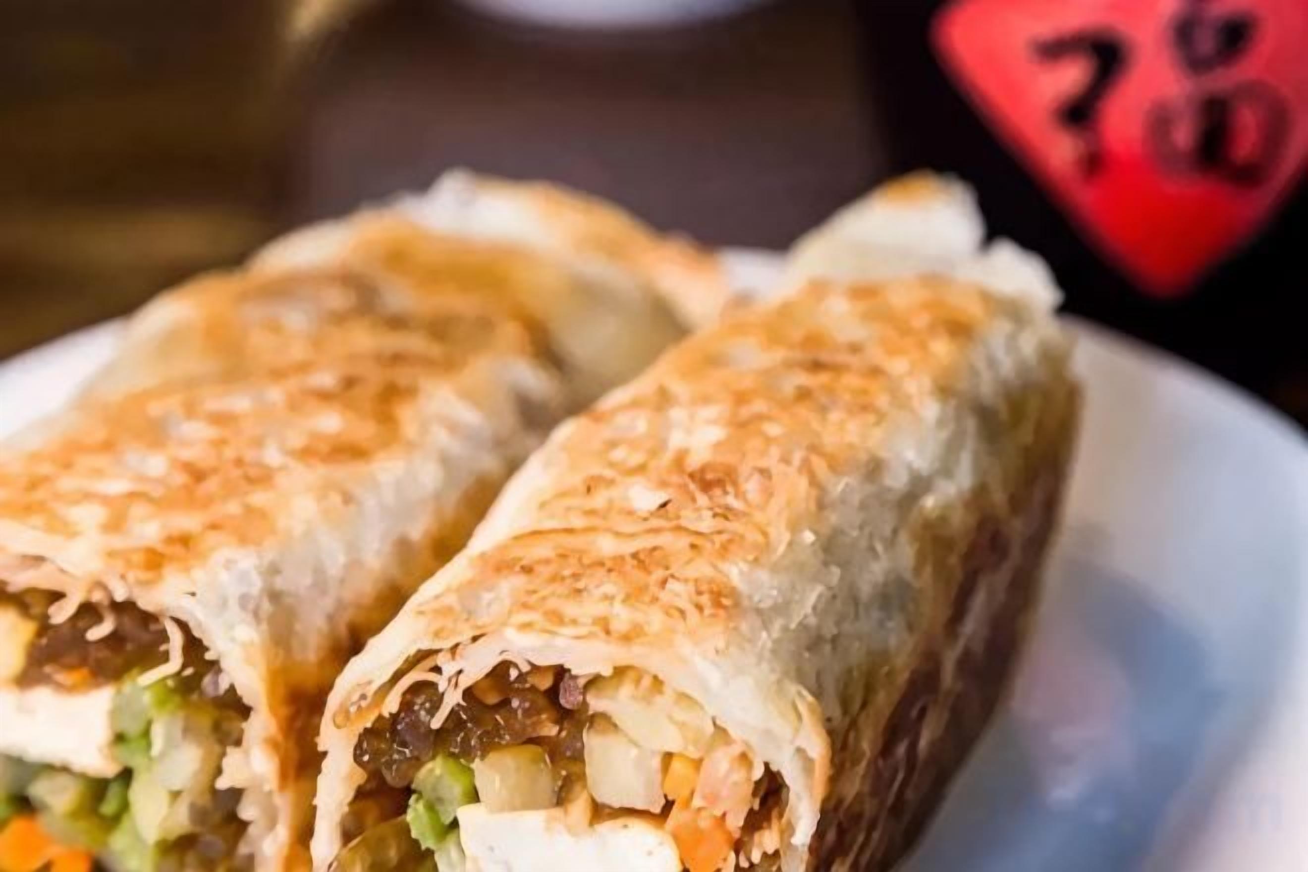 A plate with two wraps containing vegetables and possibly meat.