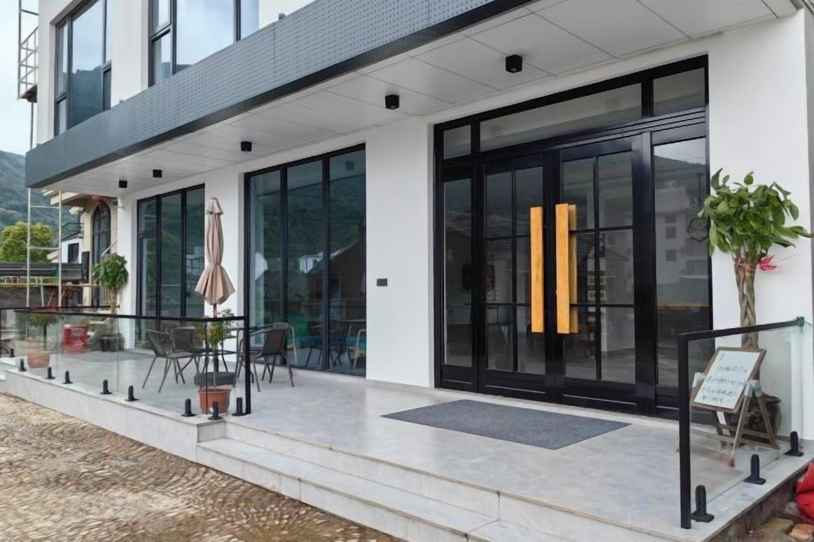 A modern building with a glass entrance, outdoor seating, and potted plants.
