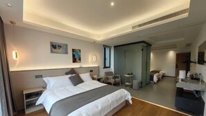 Ένα σύγχρονο δωμάτιο ξενοδοχείου με ένα μεγάλο κρεβάτι, κομοδίνα, μια μικρή γωνιά καθιστικού και έναν καθρέφτη.