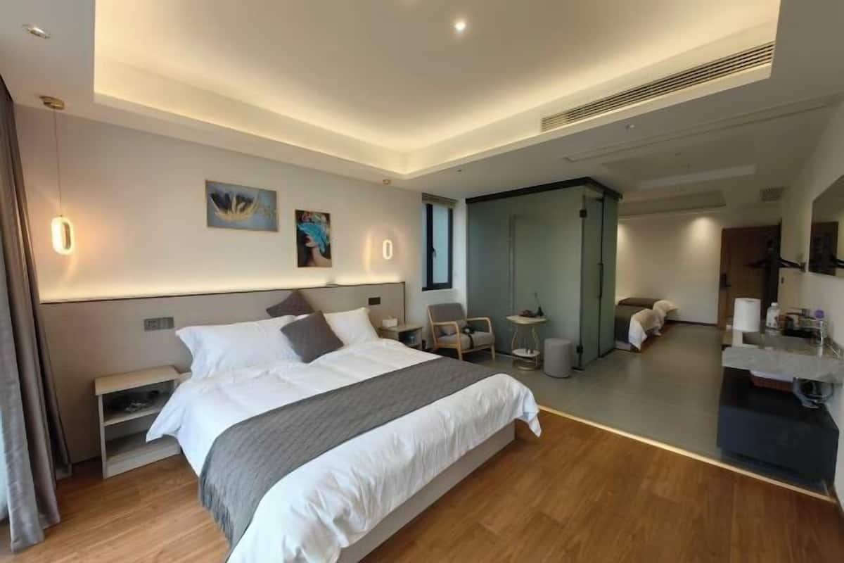 A modern hotel room with a large bed, bedside tables, a small seating area, and a mirror.
