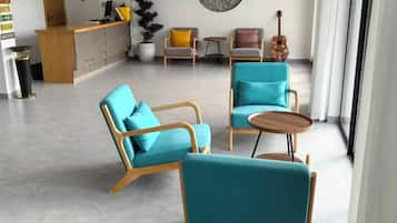 A modern lounge area with teal chairs, a wooden reception desk, and a guitar on a table.