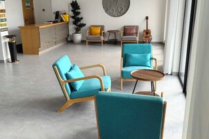 Un área de descanso moderna con sillas color turquesa, un mostrador de recepción de madera y una guitarra sobre una mesa.