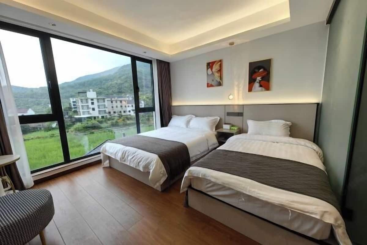 A hotel room with two beds, a large window, and a view of a building and mountains.