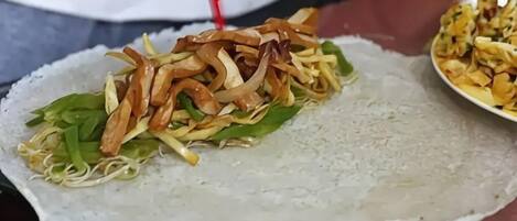Une personne prépare un plat à base de riz, de légumes et de viande sur une surface plane.