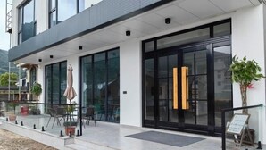 Ένα σύγχρονο κτίριο με μεγάλες γυάλινες πόρτες, εξωτερικό χώρο για καθιστικό και φυτά σε γλάστρες.