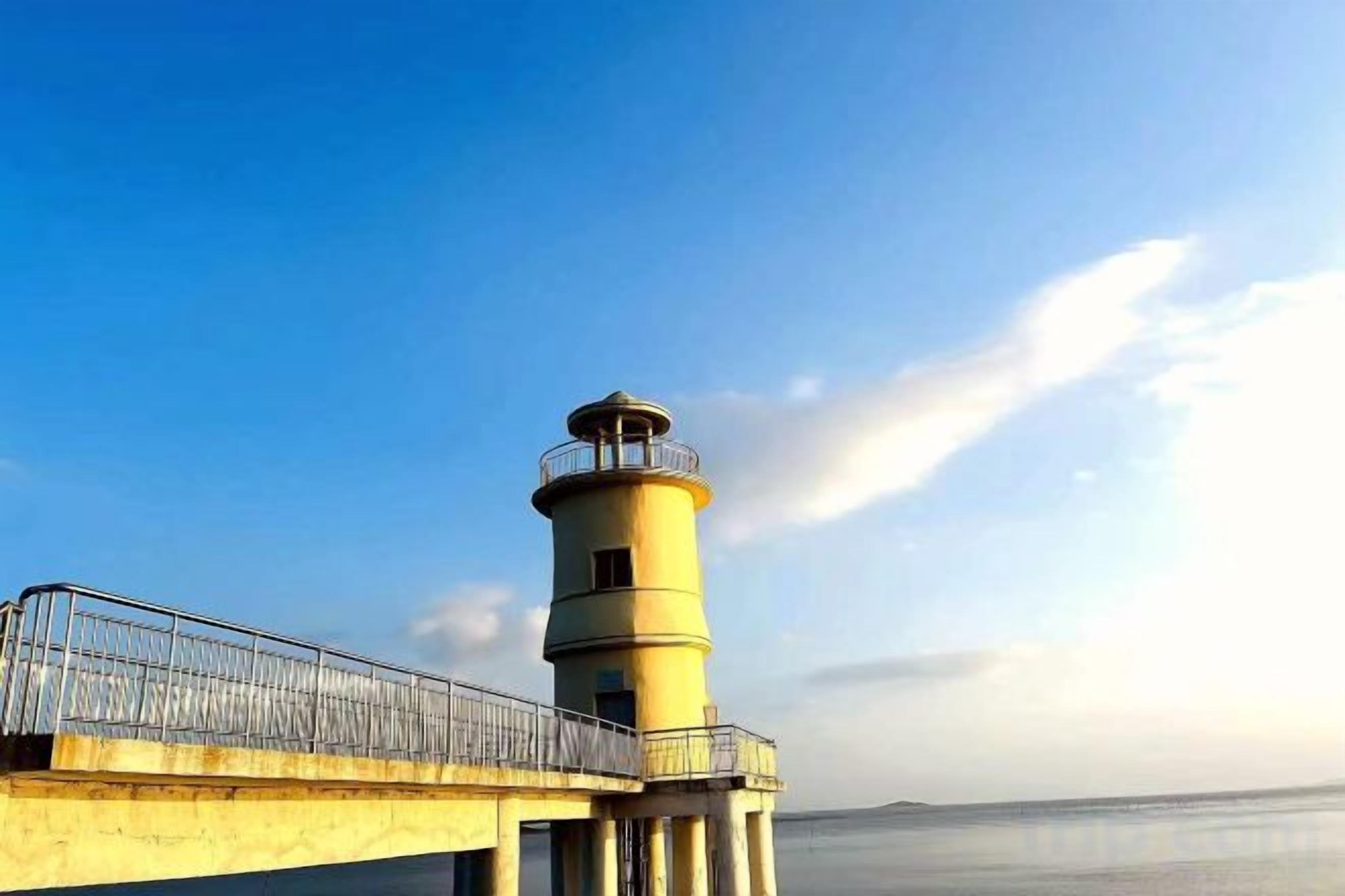 Un phare doté d’une rambarde en métal, un ciel dégagé et une eau calme.
