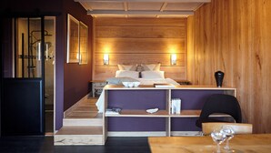 A modern bedroom with a wooden headboard, a bedside table with a book and a glass, and a chair with a glass of wine. - Thoreau Suite - A Large Studio With Mountain Views (Aramits / Pyrénées Atlantiques)
