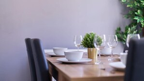 Ein Esstisch, gedeckt mit weißen Schüsseln, Weingläsern und einem kleinen Topfpflanzen.
