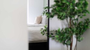 Ein Zimmer mit einem Bett, einer Pflanze und einer weißen Wand.