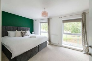 A bedroom with a large bed, a green accent wall, a window with curtains, and a ceiling light fixture.