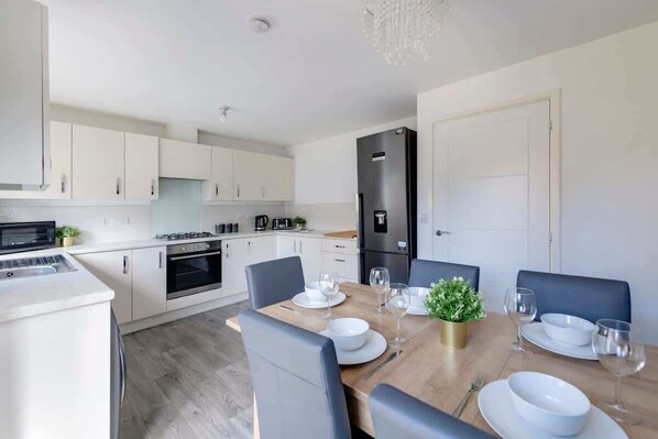 A modern kitchen with white cabinets, a dining table set for four, and a built-in oven.