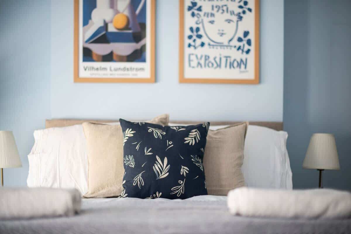 A bed with white linens, a dark pillow with leaf patterns, and two wall-mounted lamps.