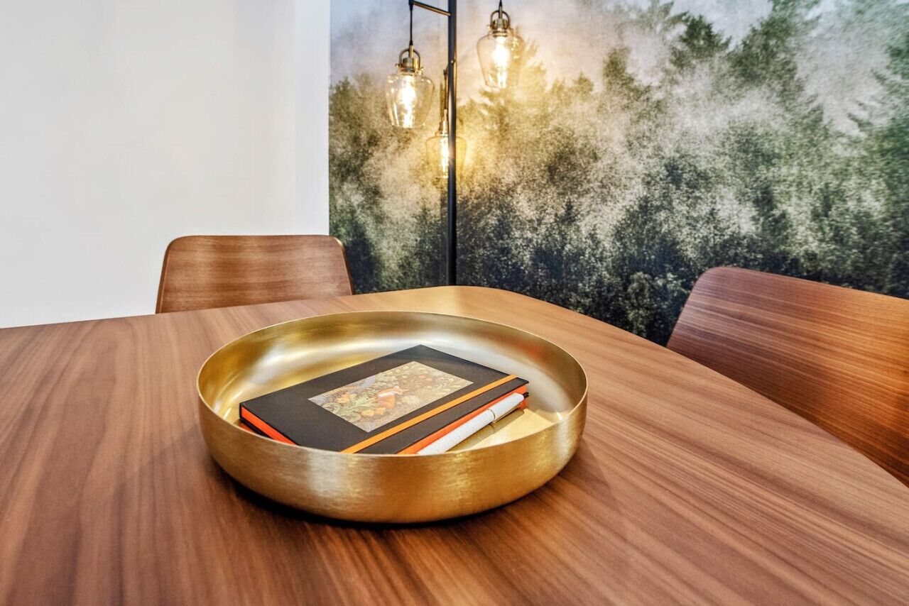 A wooden dining table with a brass tray holding books and a candle.
