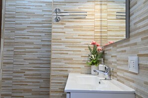 A bathroom with a tiled wall, a sink, a mirror, and a towel rack. - Villa Gioia in Costa Rei (Muravera)