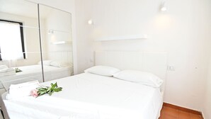 Une chambre d’hôtel propre et blanche, avec un grand lit, un miroir et une table de chevet.