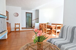 A living room with a sofa, a dining table, chairs, a wicker coffee table, and a vase with flowers. - Villa Gioia in Costa Rei (Muravera)