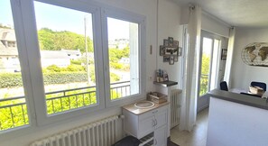 A room with large windows, a radiator, a small sink, and a shelf with items.