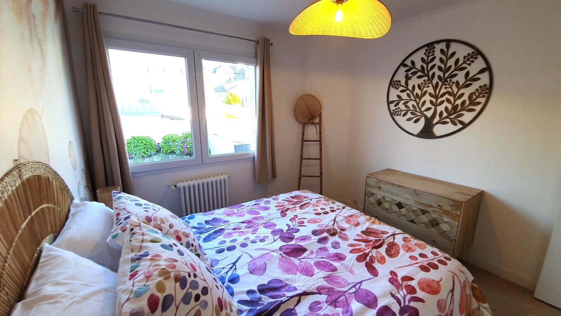 Ein Schlafzimmer mit Bett, Fenster, Heizkörper, einem Holzk dresser und einem Wandbild.