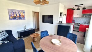 A living room with a sofa, a coffee table, and a TV. There's a kitchen with red cabinets and a stove. - flat with two bedrooms, walking distance from the beach with parking and balcony (Perros-Guirec)