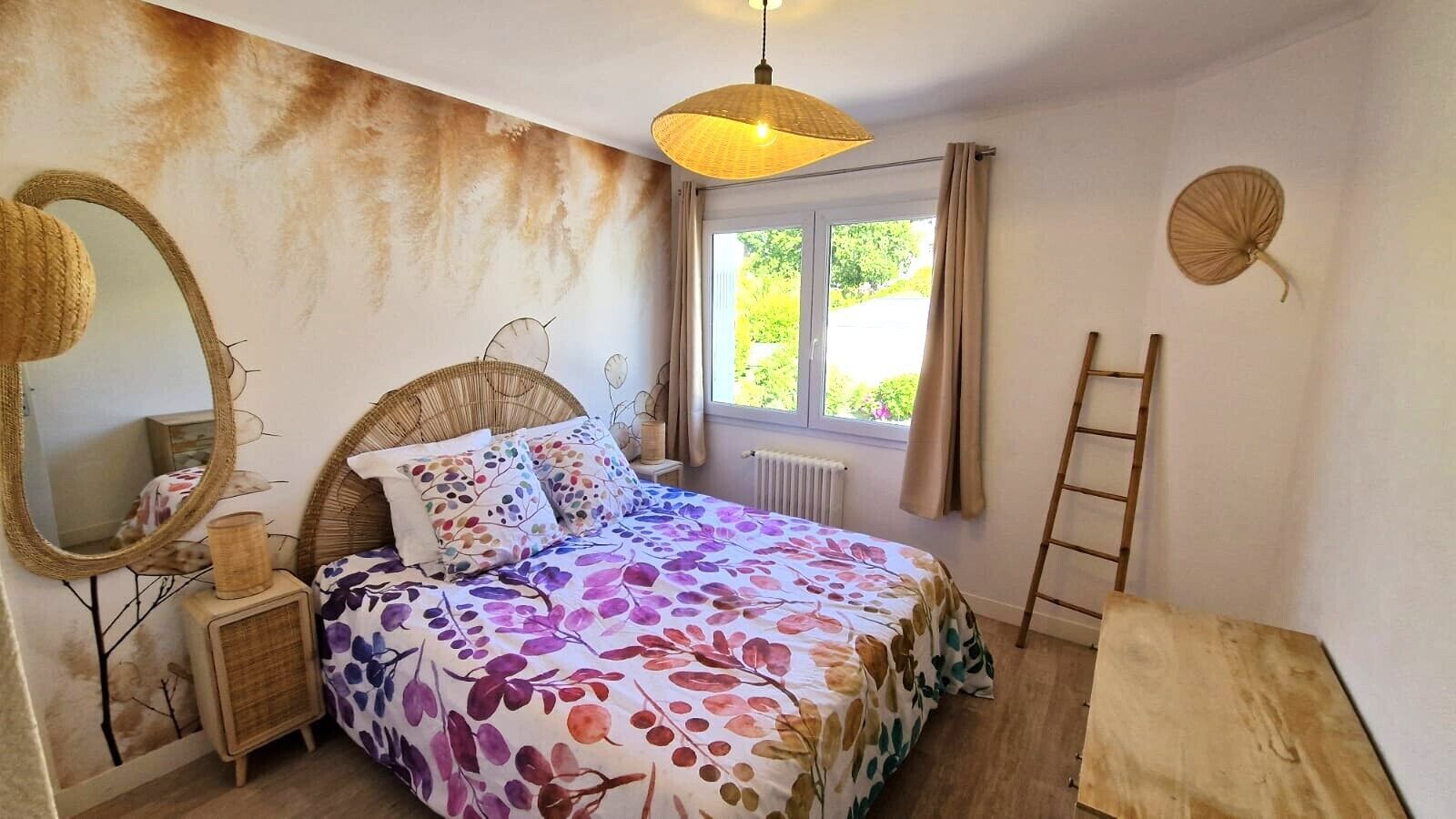 A bedroom with a bed, a bedside table, a lamp, a window with curtains, a mirror, and a ladder.