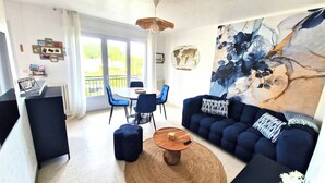 A modern living room with a sofa, coffee table, and chairs. There is a dining table with chairs, a large window, and a painting on the wall. - flat with two bedrooms, walking distance from the beach with parking and balcony (Perros-Guirec)