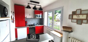 A kitchen with red cabinets, a stove, a sink, and a window with a view of houses. - flat with two bedrooms, walking distance from the beach with parking and balcony (Perros-Guirec)