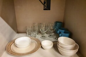 Ett förvaringsutrymme med staplade tallrikar, skålar och glas, varav några ligger i en blå behållare.