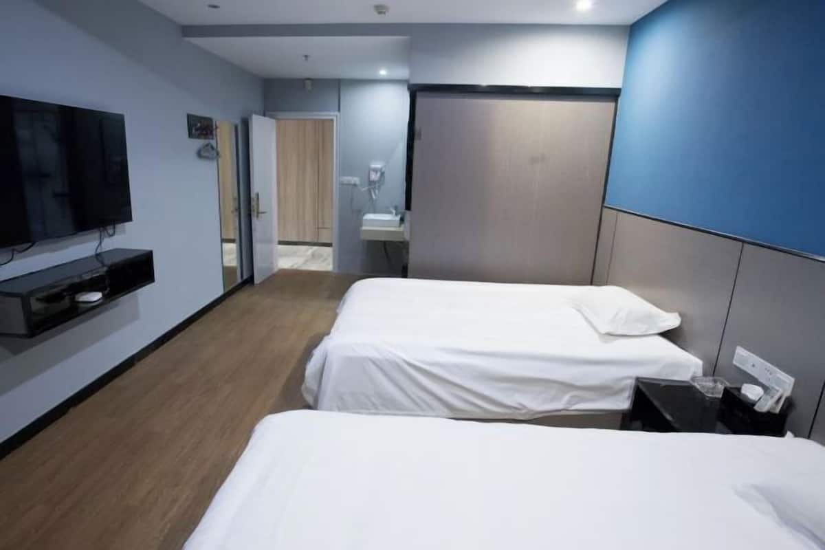A hotel room with two beds, a TV, a small table, and a bathroom visible through an open door.