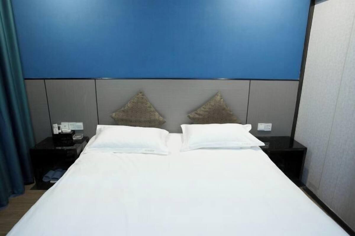 A hotel room with a bed, two nightstands, a blue wall, and a grey headboard.