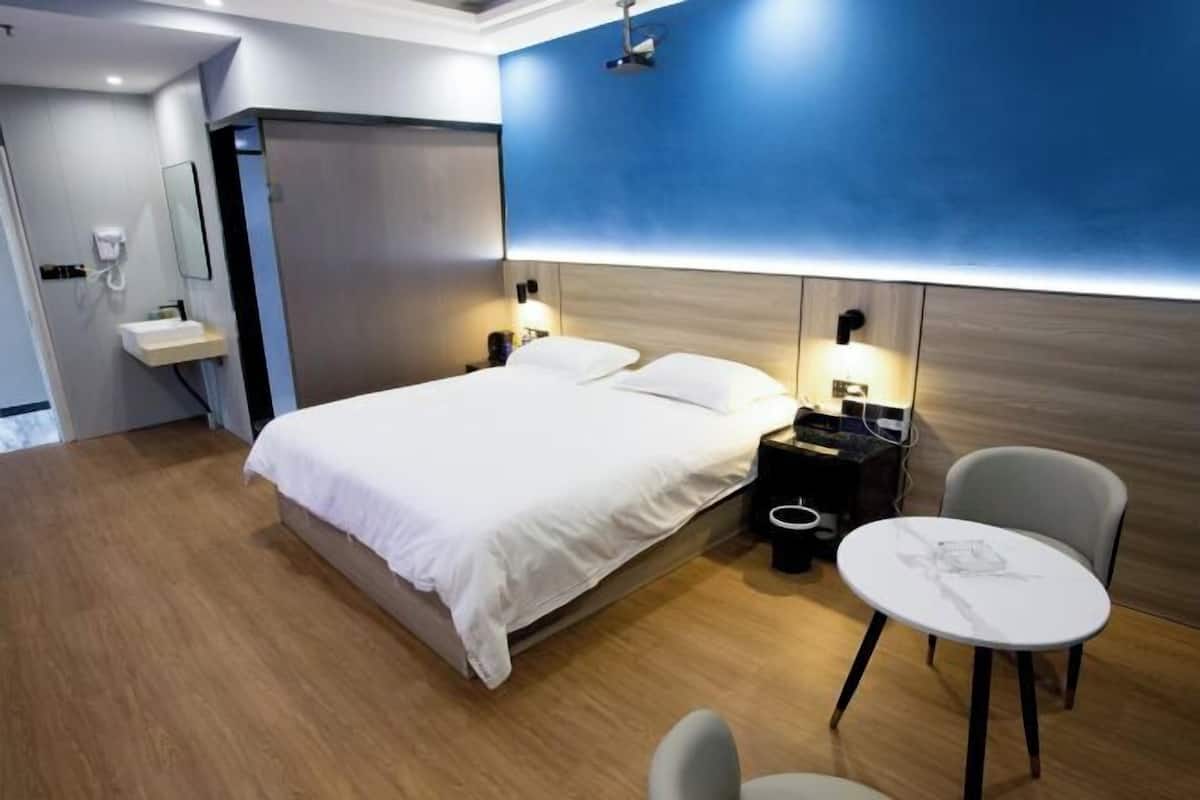 A hotel room with a bed, bedside tables, a desk, a chair, a small table, a mirror, and a phone.