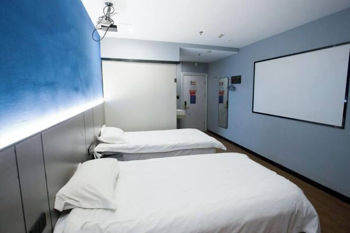 A hotel room with two beds, a large window, a whiteboard, and a door leading to a bathroom.
