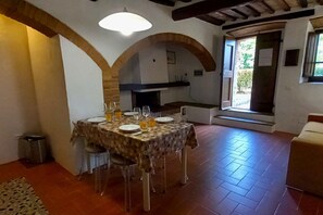 Un coin repas avec une table dressée pour quatre personnes, une cheminée et une vue dégagée sur l’extérieur grâce à une porte ouverte.