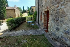 Un bâtiment en pierre avec un petit jardin, un chemin pavé et une table entourée de chaises.