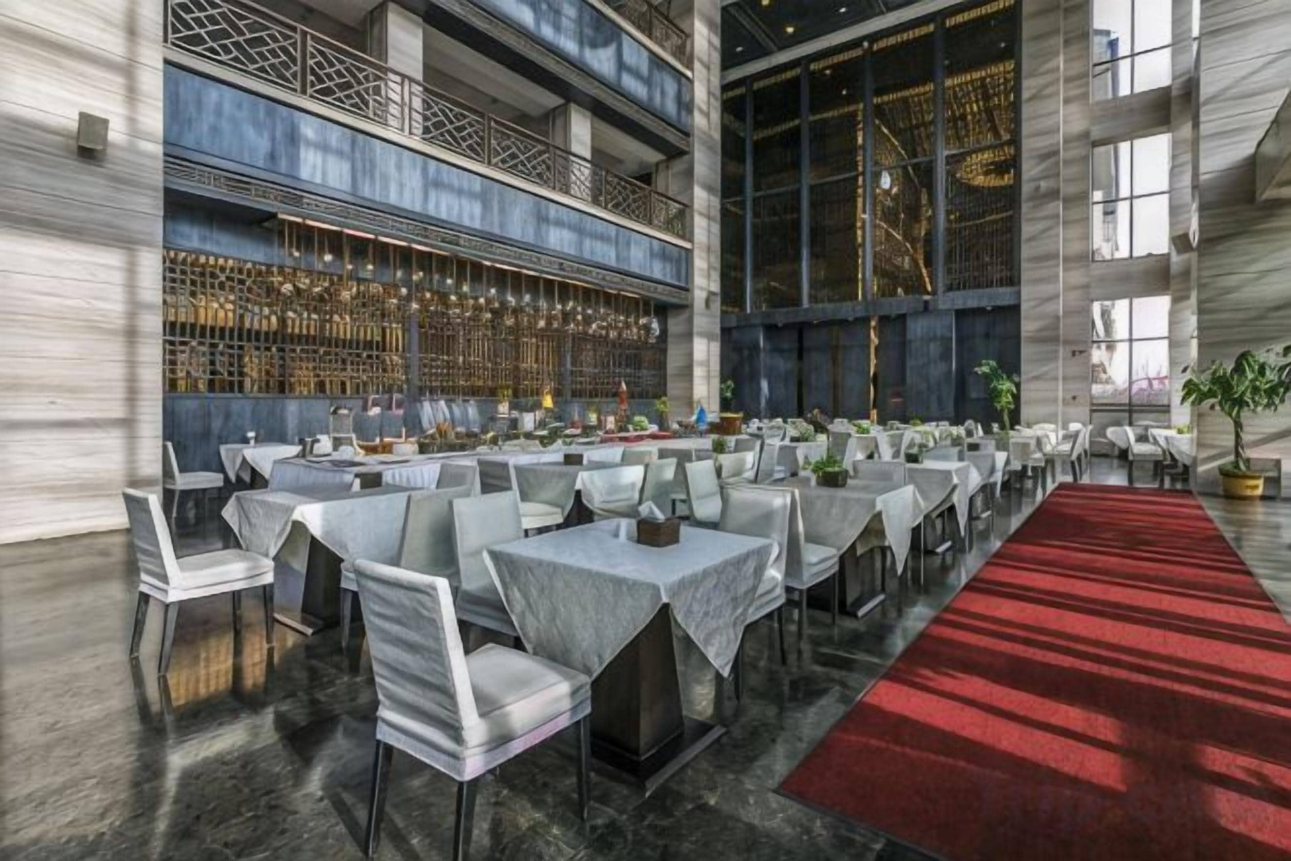 A spacious indoor dining area with multiple tables and chairs, a red carpet, and a bar with a wine rack.
