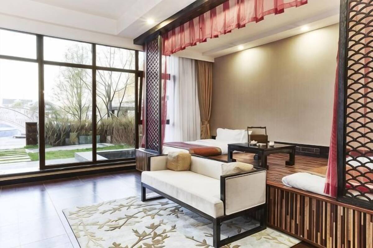 A hotel room with a large window, a sofa, a bed, and a small table.