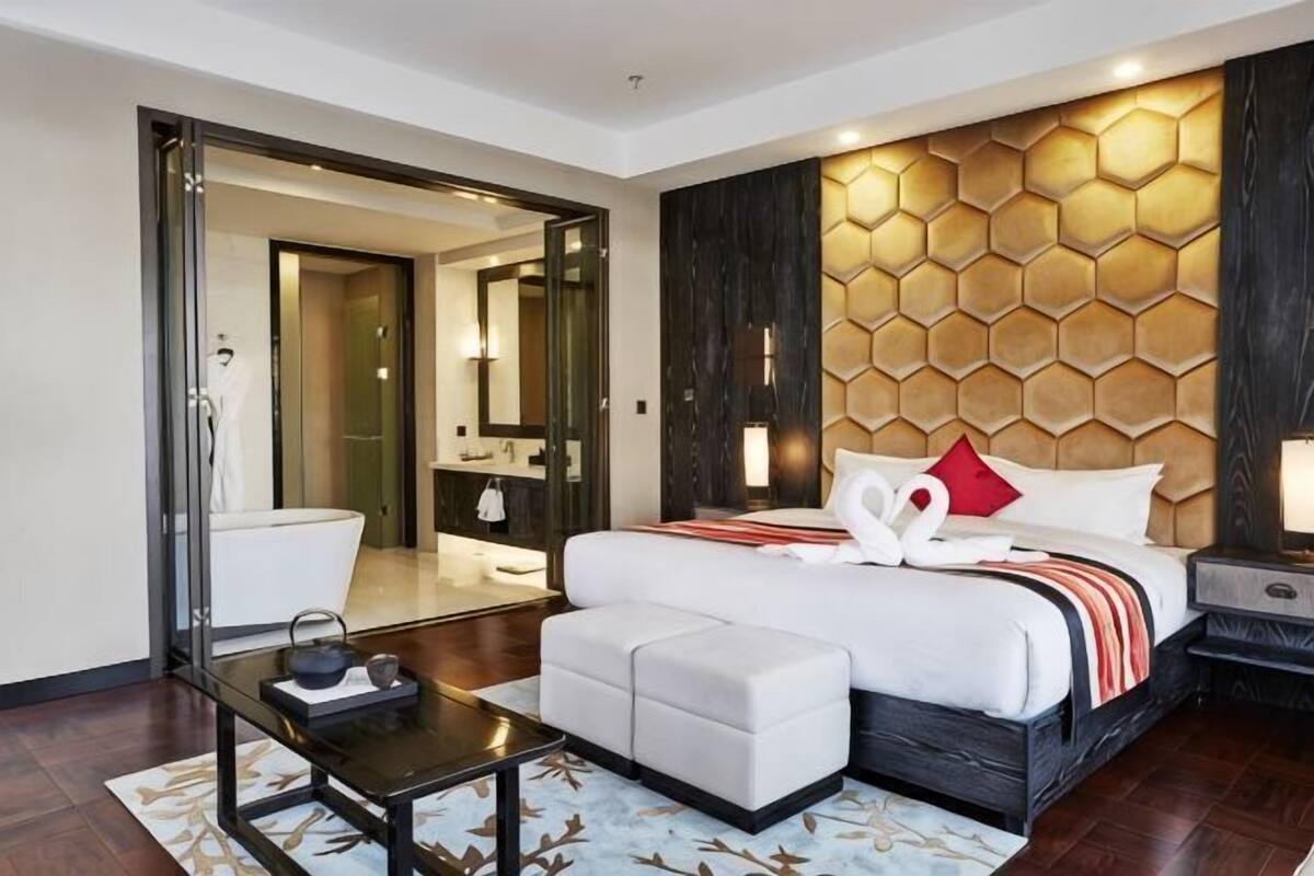 A modern hotel room with a large bed, a small sofa, a bedside table, and a mirror.