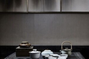 Una mesa con varios juegos de té y una tetera, sobre un fondo oscuro.