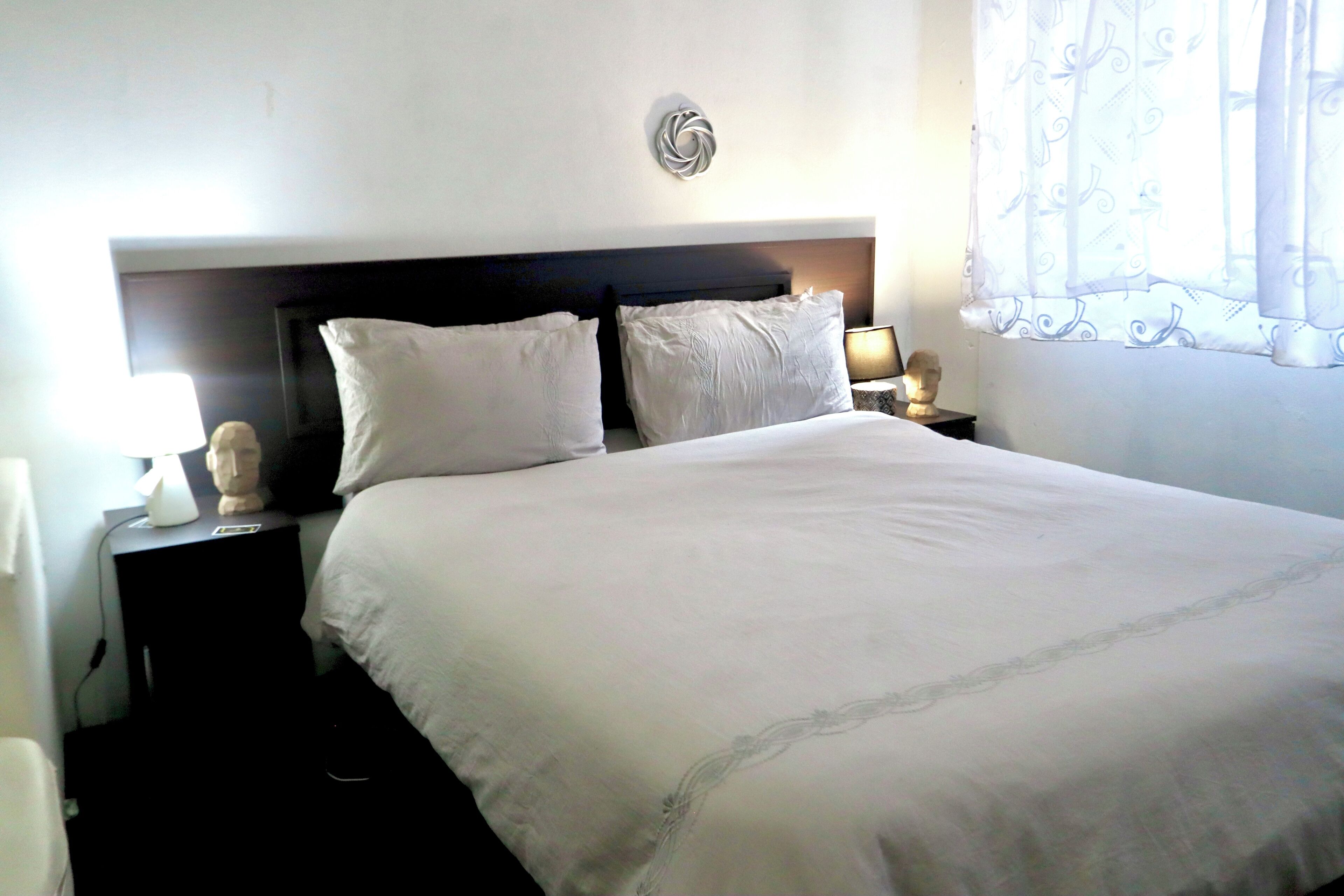 A neatly made bed with white linens, a bedside table with a lamp, and a decorative wall piece above the bed.