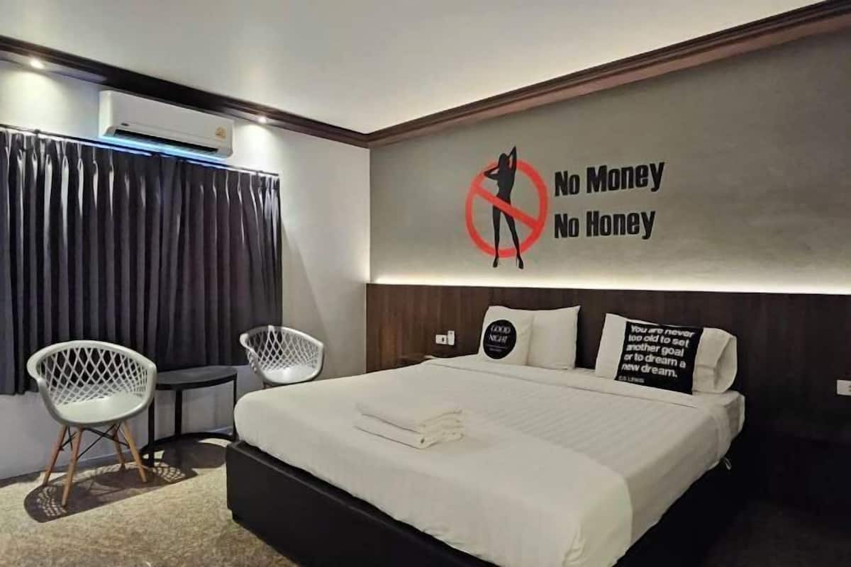 A modern hotel room with a large bed, two white chairs, a wall-mounted air conditioner, and motivational wall art.